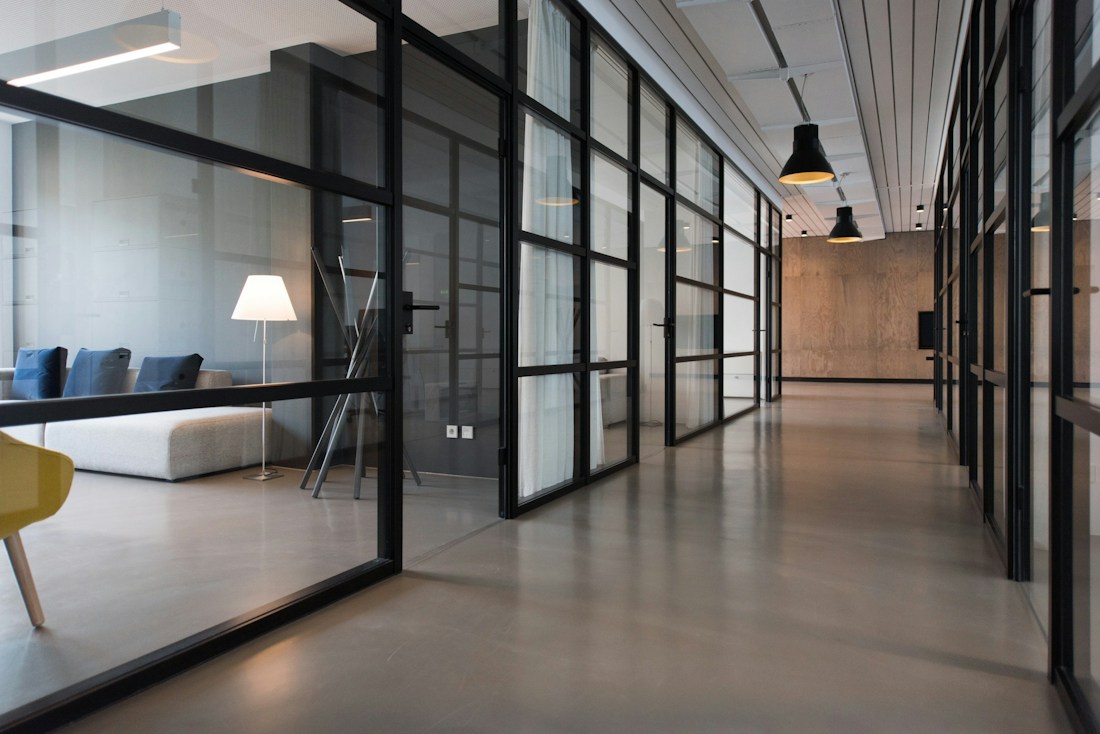 Un couloir de bureaux calme, bordé de cloisons de verre et baigné de lumière naturelle.